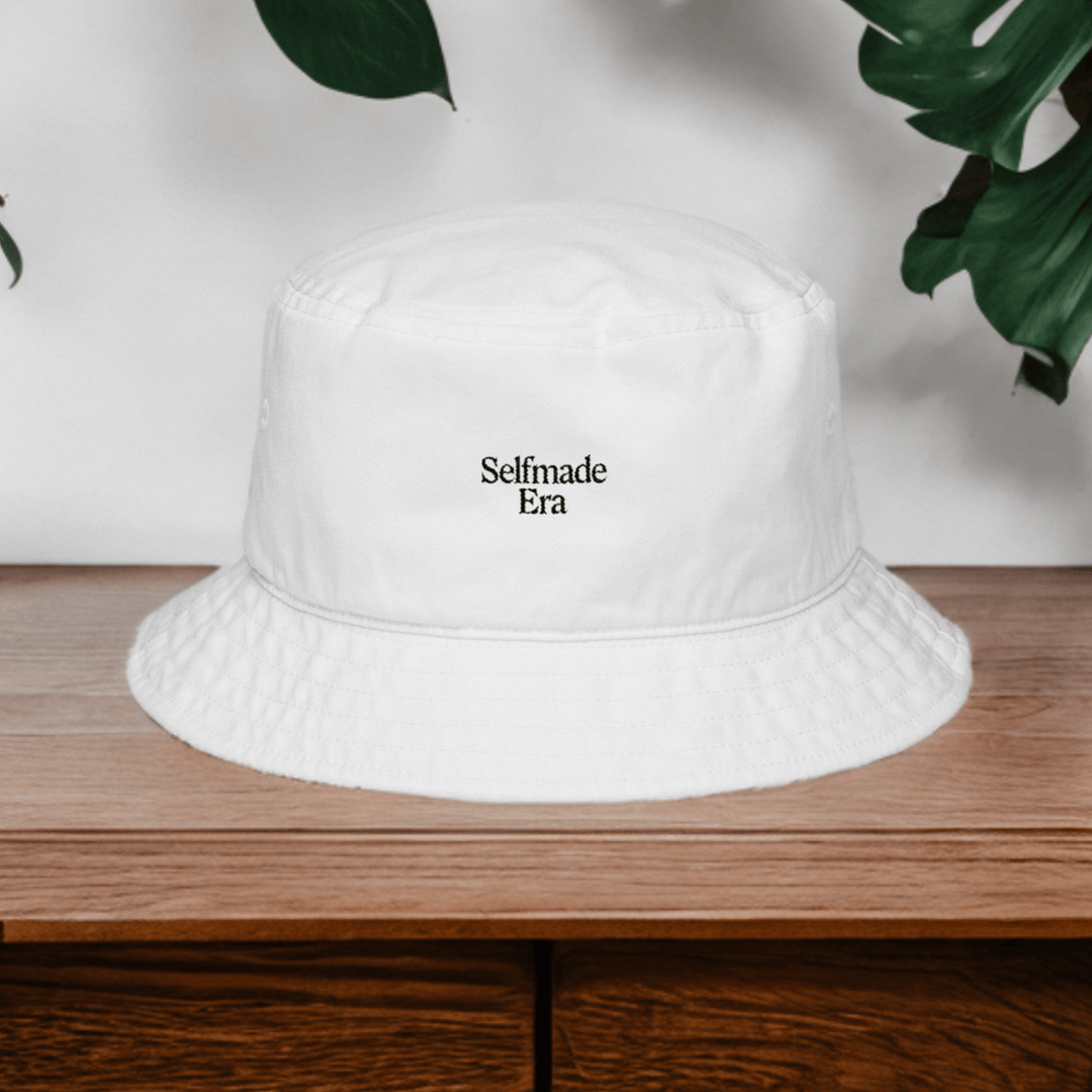 Era Embroidered Hat - Selfmade EraHatsSelfmade EraWhite Selfmade Era bucket hat placed on a wooden surface with green leaves, ideal for urban fashion and festival wear.